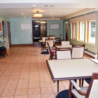An empty dining area with tables and chairs, featuring large windows and a tile floor.