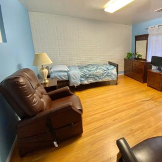 A cozy bedroom featuring a bed, recliner chair, and a TV stand.