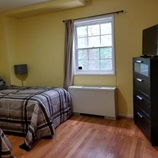 A cozy bedroom with a bed, dresser, and a window letting in natural light.