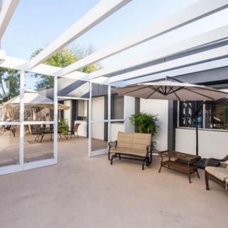 A modern patio with comfortable outdoor seating under a pergola and an umbrella, complemented by plants.