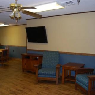 A cozy lounge area with blue chairs, wooden tables, and a flat-screen TV on the wall.