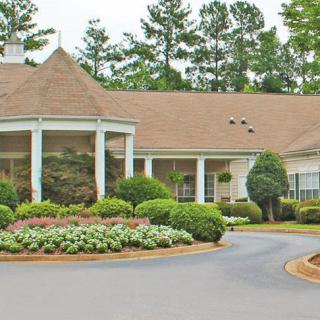 A large house with a circular driveway surrounded by well-maintained landscaping, including trees, shrubs, and flowers.