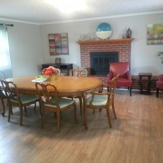 A cozy dining room featuring a large wooden table with chairs, positioned near a brick fireplace.