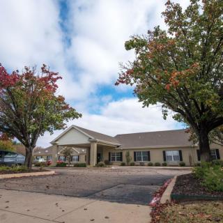 A single-story building with a parking lot surrounded by trees under a cloudy sky.