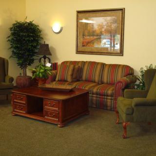 A cozy living room with a striped sofa, two armchairs, a wooden coffee table, and decorative plants.