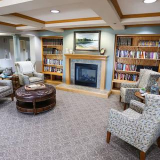 A cozy library room with a fireplace, bookshelves, and comfortable seating.