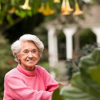 An elderly woman in a pink sweater enjoying her time in a lush garden.