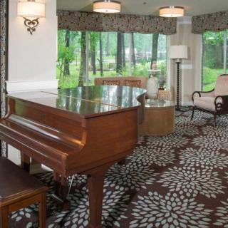 A cozy living room with a grand piano and large windows overlooking a garden.