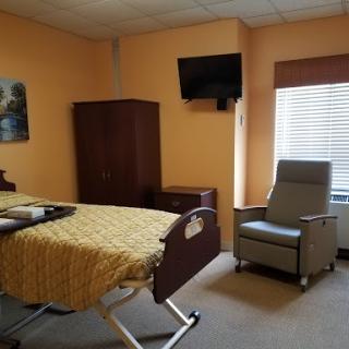 A cozy hospital room featuring a patient bed, television, and recliner chair.