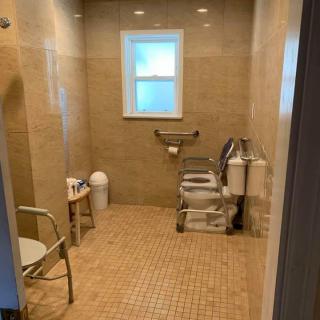 An accessible bathroom featuring grab bars, a chair, and a window.