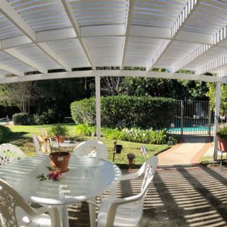 A serene patio area with a table and chairs, overlooking a lush garden and a pool in the background.