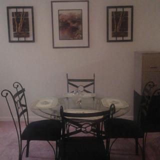 A dining area with a glass table and four chairs, accented by framed artwork on the wall.