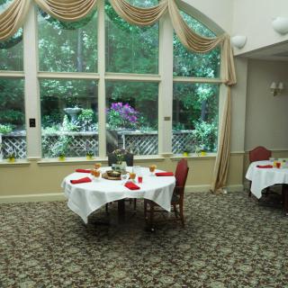 An elegantly decorated dining room with tables set for guests, featuring large windows overlooking a garden.
