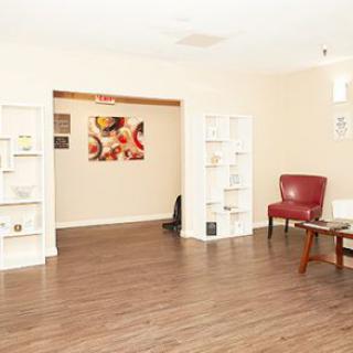 A bright living room with wooden flooring, featuring a red chair, bookshelves, and colorful artwork on the wall.