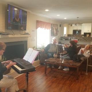 A group of people in a living room, enjoying music played on a piano while seated comfortably.