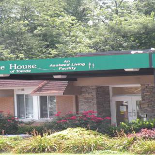 A building with a green sign indicating it is an assisted living facility, surrounded by landscaping and flowers.
