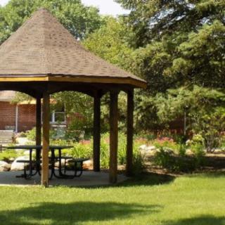 A wooden gazebo in a lush green park surrounded by trees and shrubs.