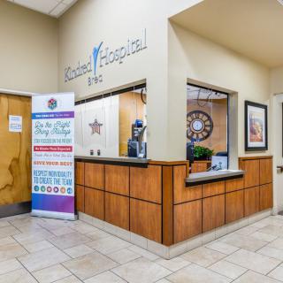 The image shows the reception area of a hospital with a front desk and informational signage.