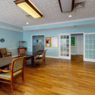 A spacious and well-lit room with wooden floors, featuring chairs, tables, and light blue walls.