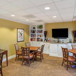 A cozy meeting room with tables, chairs, and a TV, decorated with artwork and bookshelves.