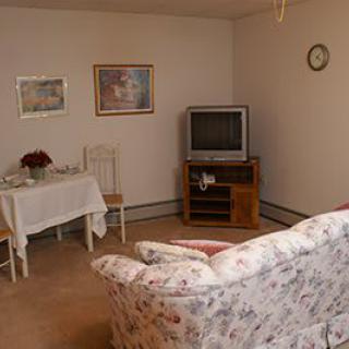 A cozy living room with a floral couch, television, dining table, and wall art.