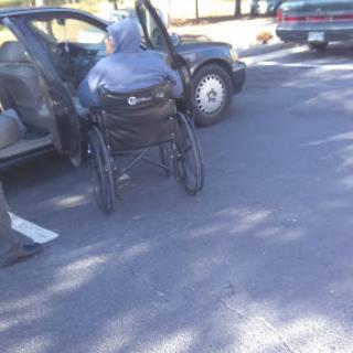 A person in a wheelchair is approaching a vehicle in a parking area.