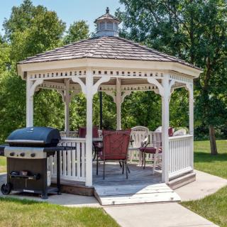 A cozy outdoor gazebo with patio furniture and a grill on a sunny day.