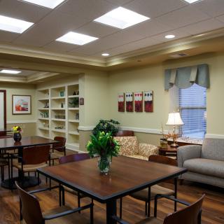A cozy library reading room with tables, chairs, and bookshelves.