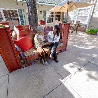 Two people sitting and talking on a patio with an umbrella.