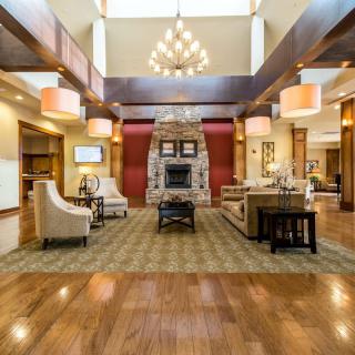 A spacious and elegantly designed lobby featuring a stone fireplace, comfortable seating, a large chandelier, and wood flooring.