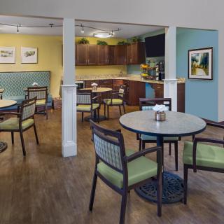 A cozy dining area with tables and chairs, featuring a kitchenette in the background.