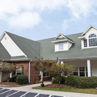 A two-story residential building with a green roof and multiple windows under a partly cloudy sky.