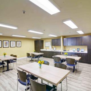 A modern office break room with tables, chairs, and a kitchen area.