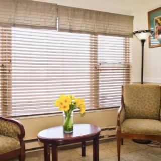 A cozy living room with two chairs, a coffee table, and bright flowers near a large window with blinds.