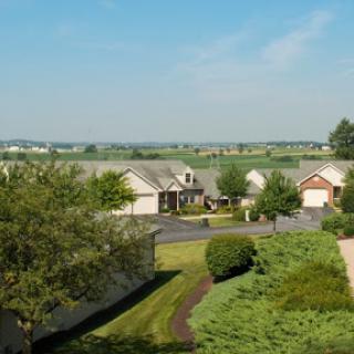 A serene suburban view featuring homes surrounded by lush greenery and a clear blue sky.