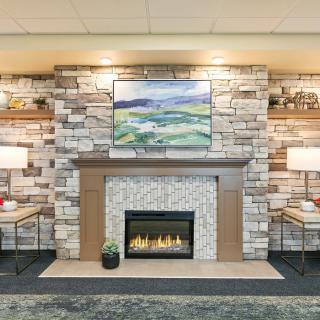 A cozy living room with a stone fireplace, adorned with artwork and flanked by stylish lamps.