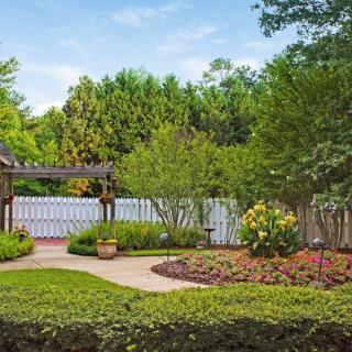 A beautifully landscaped garden with a pergola, pathway, and a variety of flowers and trees.
