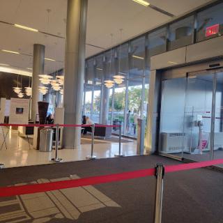 A modern lobby with glass doors and a waiting area, featuring red rope barriers.