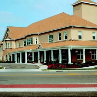A two-story residential building with columns and a red roof, seen from across the street.
