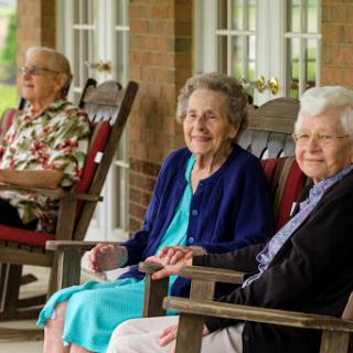 Three elderly women enjoying a moment together on a porch, sharing smiles and companionship.