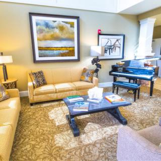 A well-decorated living room featuring beige sofas, a black grand piano, and colorful artwork on the walls.