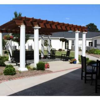 A picturesque outdoor patio area featuring a wooden pergola supported by white columns, surrounded by a well-maintained garden with seating arrangements.