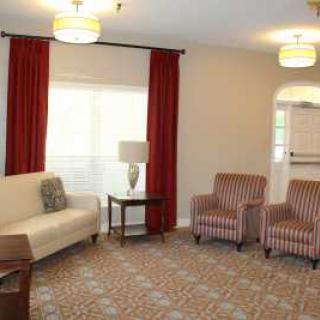 A cozy living room with a sofa, two armchairs, and red curtains.