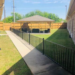 A peaceful backyard scene featuring a paved pathway leading to a gazebo, surrounded by green grass and a wooden fence.