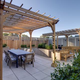 A well-designed outdoor patio with a wooden pergola, dining furniture, and surrounding garden greenery.