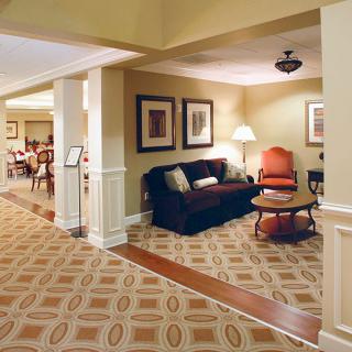 A cozy living room with a sofa, armchair, table, and lamp, complemented by framed artwork and patterned carpet.