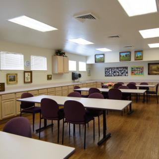 An empty classroom with tables and chairs, adorned with artwork on the walls.