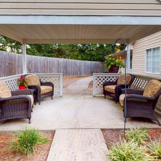 A cozy outdoor patio with wicker furniture under a covered area in the backyard, featuring a garden path and surrounded by a fence.
