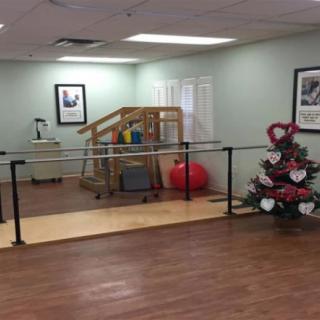 A physical therapy room with parallel bars and exercise equipment, decorated with a festive tree.