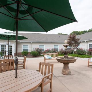 A peaceful patio area with tables, chairs, and large umbrellas surrounding a decorative fountain.